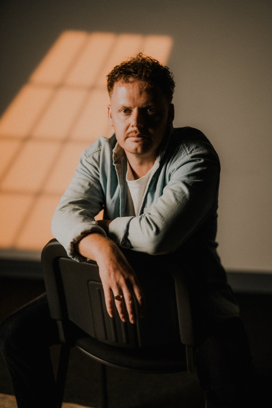 Reuben Mowle, filmmaker and photographer, sitting on a chair in warm window light
