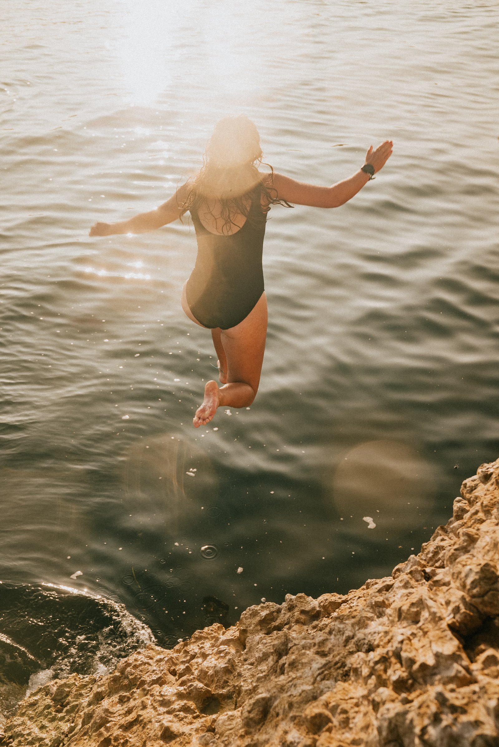A woman jumping into the water from a rock